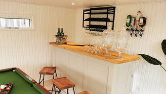 Bright garden games room with a fitted bar, drinks dispensers, glassware and a pool table.